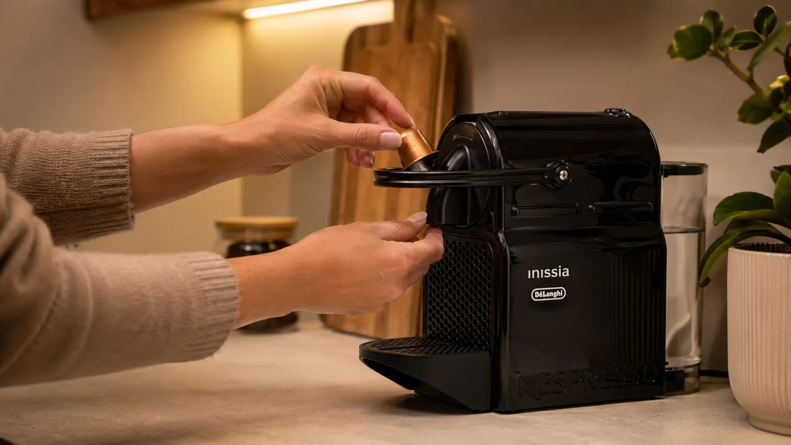 Hand pressing the espresso button on the Nespresso Inissia while a red capsule sits in the capsule holder